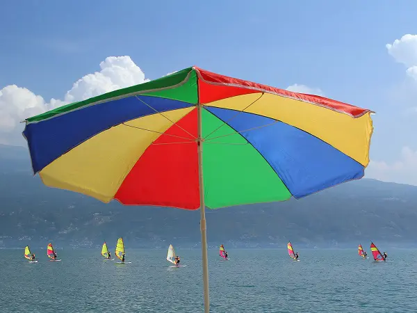 Beach umbrella in rainbow colors and group of windsurfers on gar